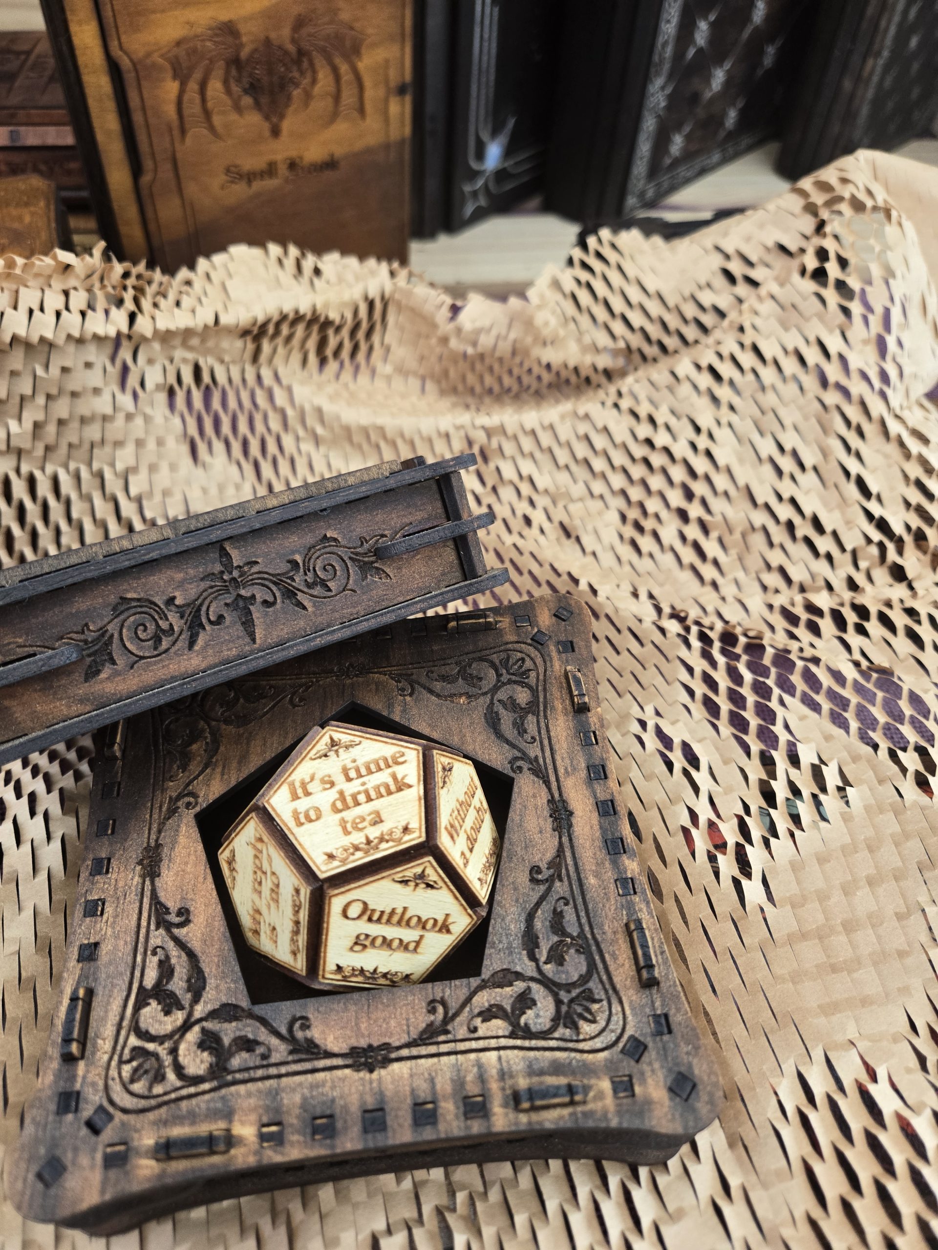 Small wooden puzzle box holding a fortune-style D10 die, featuring playful messages such as “Outlook good” and “Re-roll the dice.”