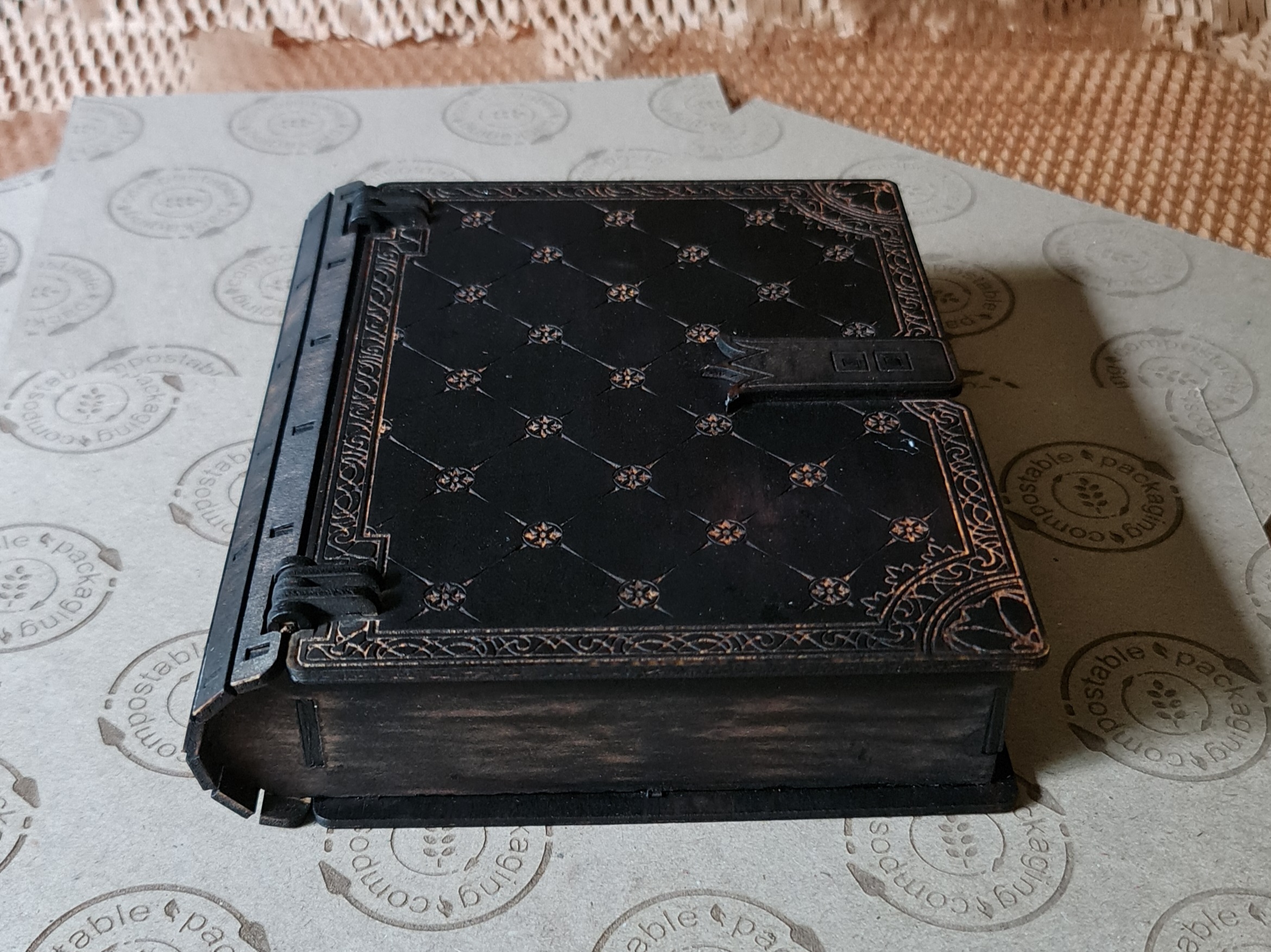 Antique-style black engraved wooden book box shown in detail, featuring ornate carved patterns inspired by classic fantasy book designs.