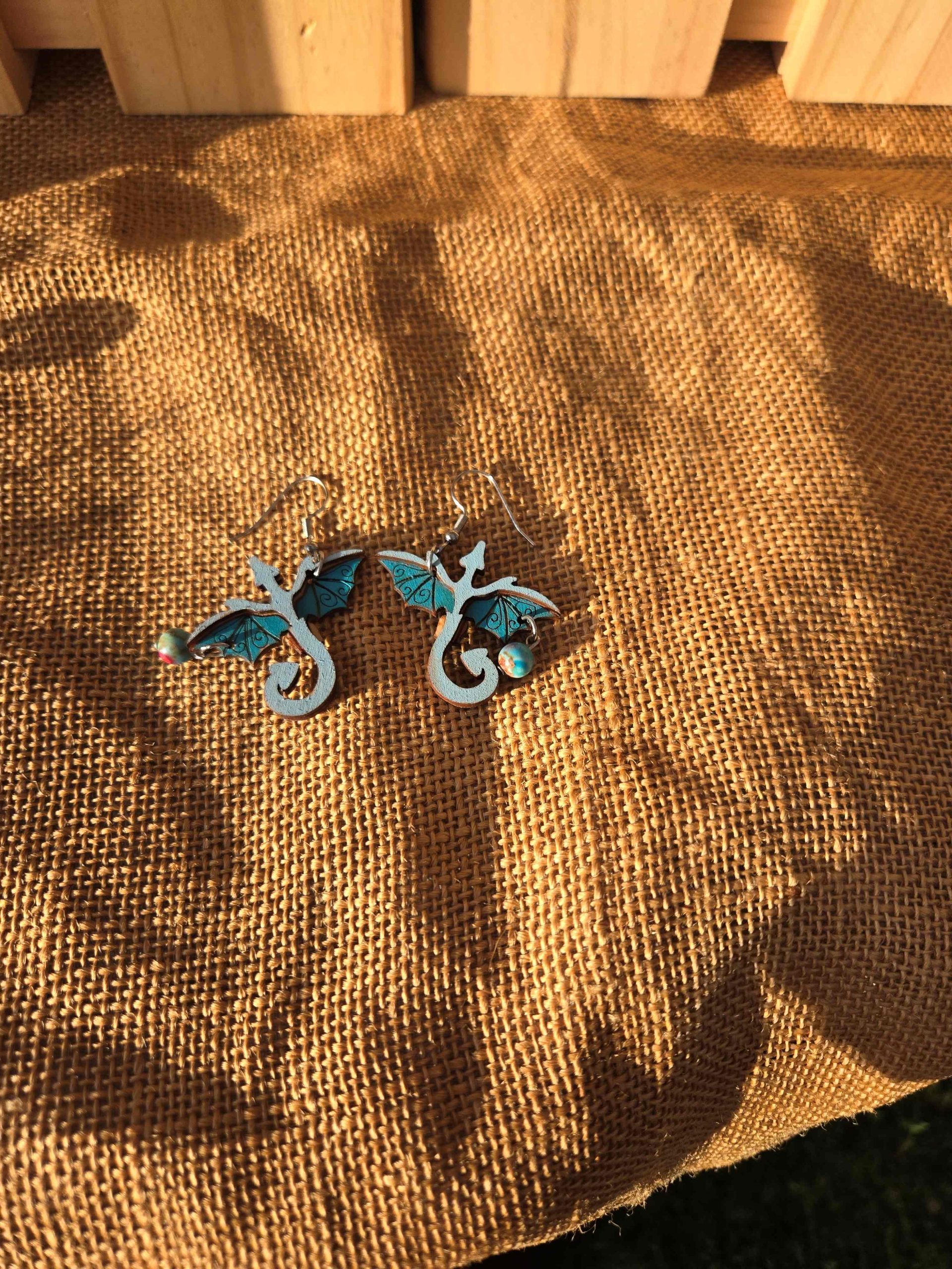 Layered wooden dragon dangle earrings with stainless steel hooks and small crystal drops, shown in natural finishes and available in multiple colours.