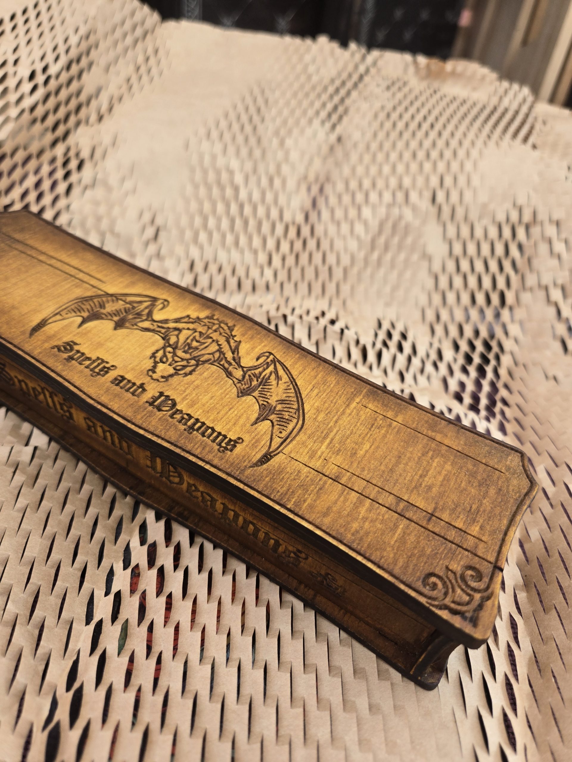 Closed handcrafted wooden long dice box engraved with spells, weapons and a dragon design on the lid.