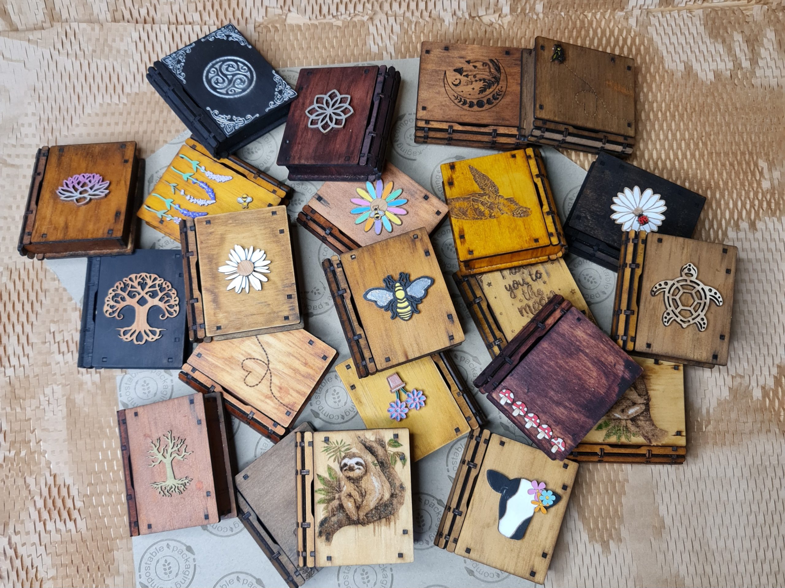 Varied collection of mini wooden gift boxes displayed together, showcasing multiple fantasy designs and engraved styles.