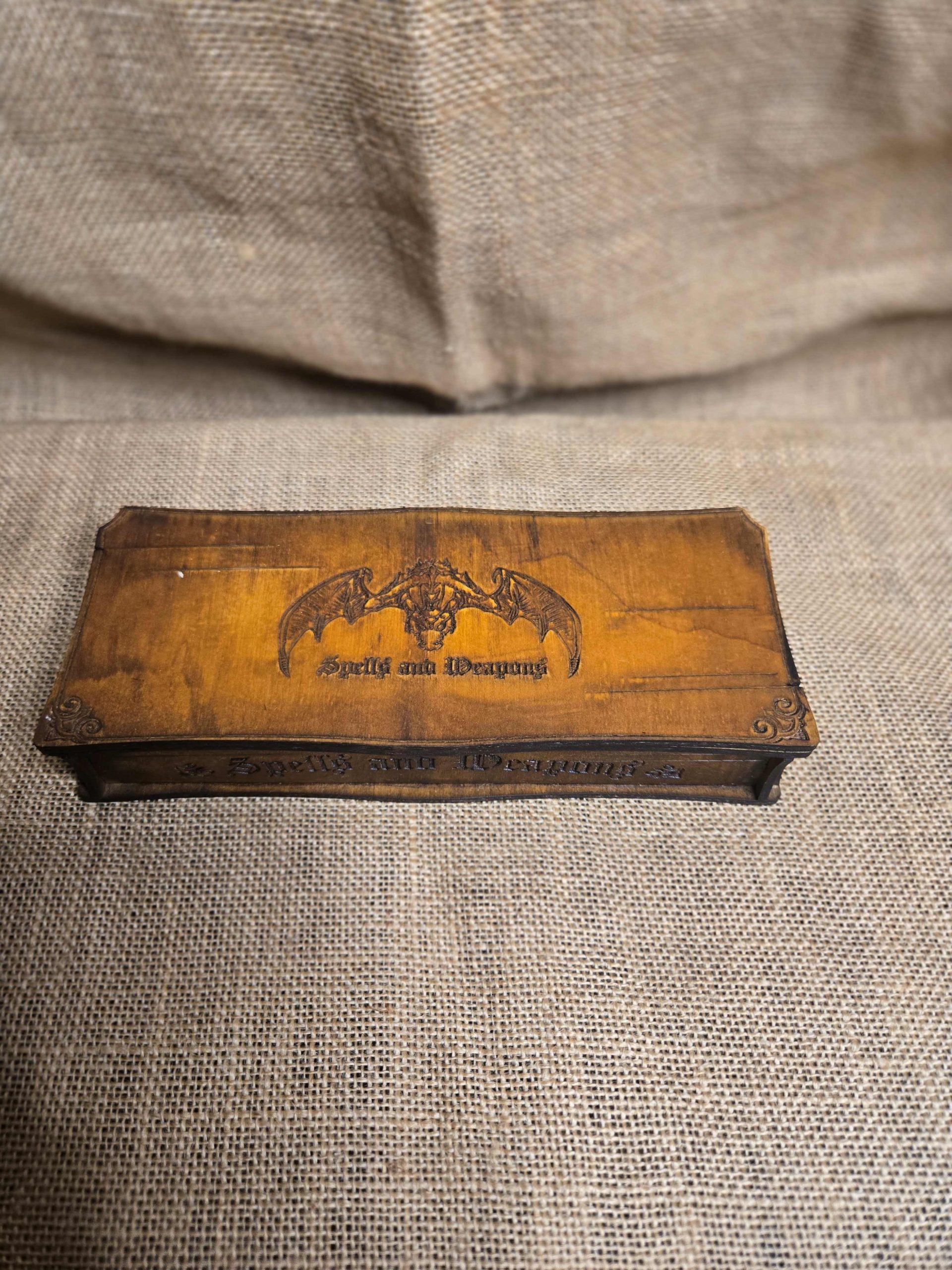 Medium-sized wooden dice box with engraved dragon, spells and weapons on the lid, shown closed.