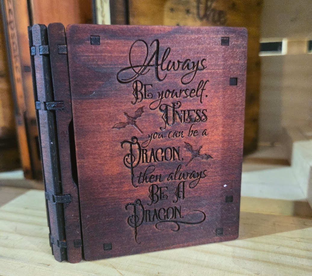 Small jarrah-stained sliding wooden book box engraved with the phrase “Always be yourself unless you can be a dragon.”