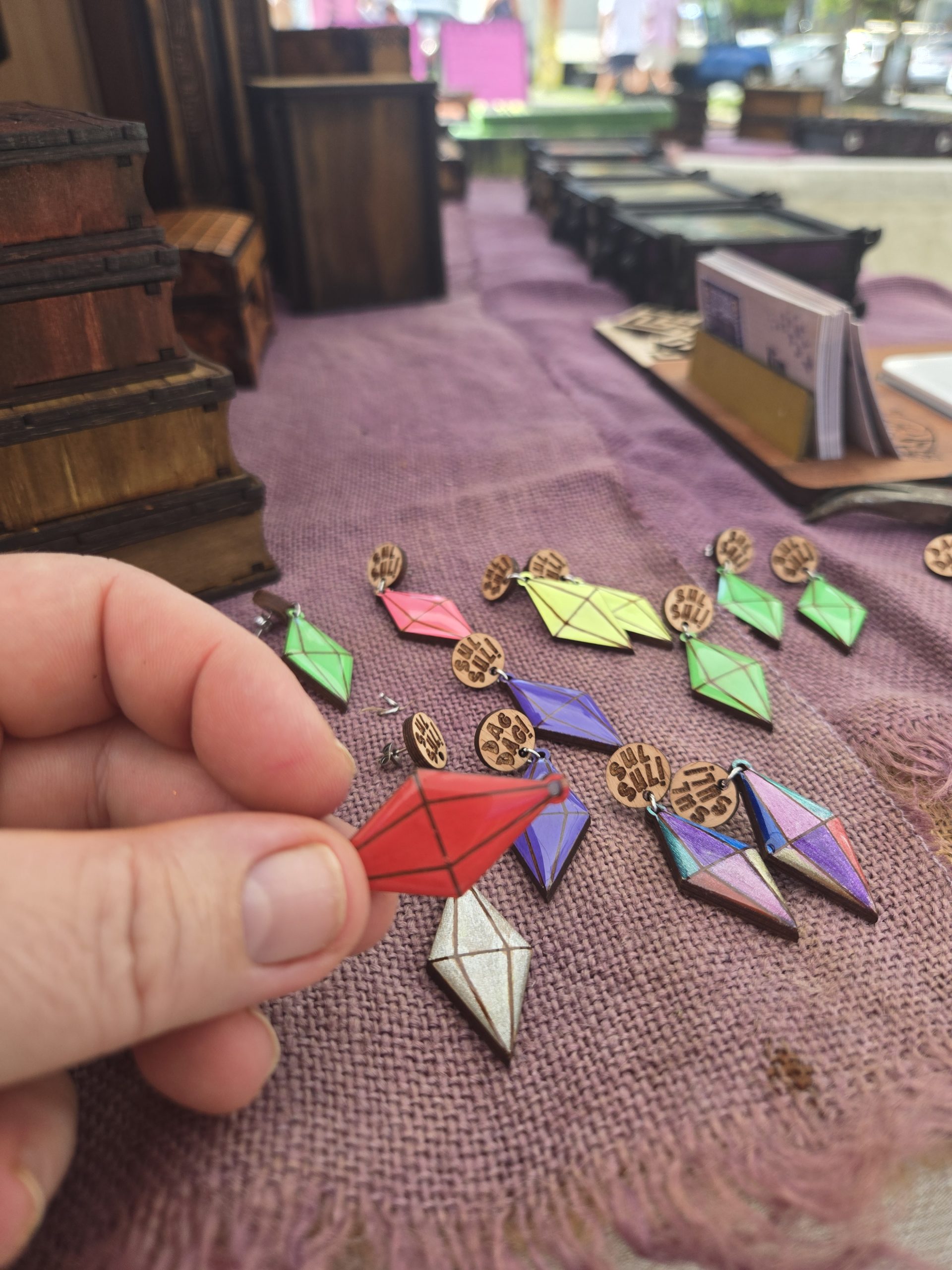 Assorted plumbob-themed earrings featuring wooden stud tops engraved with “Sul-Sul” and “Dag-Dag,” with hanging plumbob charms in various colours.